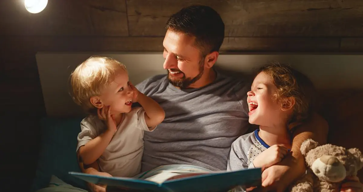 Ojciec czyta książkę swoim roześmianym dzieciom przed snem