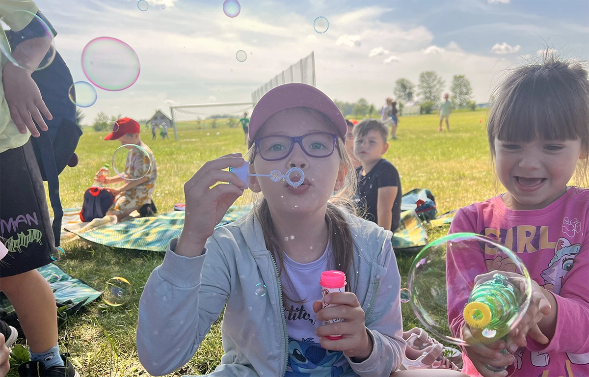 Dzieci bawią się na pikniku, dziewczynka na pierwszym planie puszcza bańki mydlane